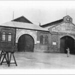 Image: A woman walks by two long brick buildings, one of which has the words ‘Edwin Daw Central Fish Market’ on its facade