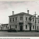 Image: a two storey corner hotel with 1960s era cars parked on the street outside.