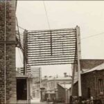 Image: A framework holding numerous cables is positioned next to a two-storey stone building. A similar framework is visible in the background