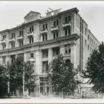 Image: a five storey stone building with a symmetrical façade under construction. There are balconies and balconets on most floors although they are of different shapes and formations, some protruding and some set into the building.