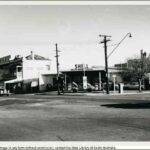 Image: A 1960s era shell service station, with a car with its bonnet up parked under the overhanging roof, sits on the corner of two city streers