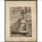 Image: Photograph of cross shaped headstone beside a church