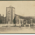 Image: A low, squat church building stands at the intersection of two dirt roads. A man stands in front of the fence bordering the churchyard