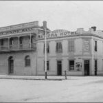 Image: A white, two-storey building stands at the corner of two dirt streets. The words ‘Aurora Hotel’ are painted on the side of the building