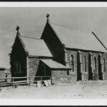 Image: A stone church with a steep peaked roof stands in an open expanse of flat ground