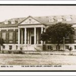 Image: A large rectangular brick building with Greek Revival-style columns flanking its main entrance