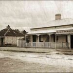 Image: two girls stand in front of their respective cottages while geese peck in the gutter before them. One cottage is in a state of disrepair .