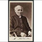 Image: Photograph of bald seated man wearing a dark coloured coat and clerical collar