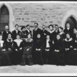 Image: men and women in dark coloured clothing pose in two rows for a formal photograph.