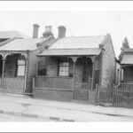 Image: a row of tiny stone workers cottages with brick quoins, a single door and window beneath a verandah on the front elevation, pitched tin roofs and small lean-tos on the rear.