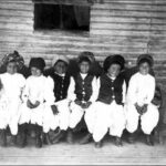 Image: A group of children in traditional Afghan clothing sit on the verandah of a rural home