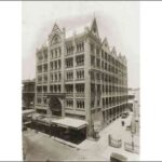 Image: a seven storey gothic style building with a large decorative arch over a protruding verandah on one side, and a line of gable roofs.