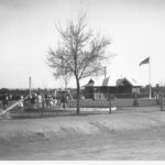 Image: Several children play at a playground with a large shelter, flagpole and equipment