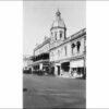 Image: a two and three storey terrace featuring a large octagonal tower with a cupola, a verandah with awnings and arched windows and balconets on the right of the building and a larger balcony on the left.