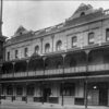 Image: a large three storey building with a relatively simple design including a balcony, parapet and waist height tiling along the bottom of the building.