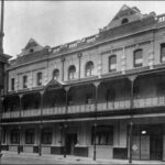 Image: a large three storey building with a relatively simple design including a balcony, parapet and waist height tiling along the bottom of the building.