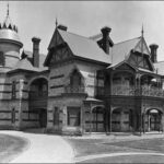 Image: A large, two-storey stone mansion with a cylindrical turret comprising one corner of the structure