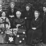 Group of women sitting down in foreground with flag, women standing in background