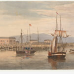 Image: A number of sailing ships are moored in a river. A scattering of buildings and a wharf are visible in the background