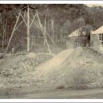 Image: Two single-storey stone buildings stand next to large dirt piles and a wooden tower