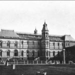 Image: A large, two-storey stone building with a central tower and several large, arched windows