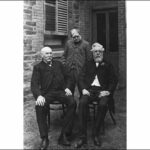 Image: Three elderly Caucasian men in late Victorian-era attire pose for a photograph outside a bluestone building. Two are seated while another stands.