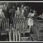 Image: A small group of women stand in a room with several unfinished artillery shells