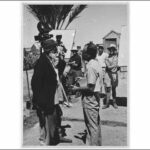 Image: A group of Caucasian men with film equipment observe a conversation between two other men, one of whom is elderly and dressed in Afghan attire