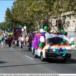 Image: women carrying banners and holding green and purple balloons march down a city street following a van decked out in balloons, bows and swathes of coloured fabric. One of the women near the front is beating a large drum