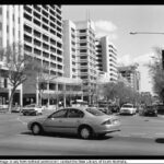 Image: late 1990s and early 2000s cars wait at an intersection of a street lined with skyscrapers