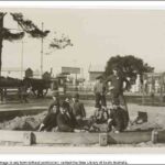 Image: A group of children play in a sandbox in a park. A street and buildings are visible in the background