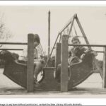 Image: Two boys sit in a ‘rocking boat’ at a playground. A swings-set is positioned immediately behind the boys