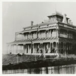 Image: large two story building with smaller third story and wrap around verandah