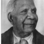 Image: A photographic head-and-shoulders portrait of an elderly Aboriginal man. He is clean-shaven, sporting a short haircut and is wearing a suit jacket and tie