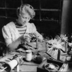 Image: A young woman sits at a table and works on a circular device held in a mounting. The table is covered with several similar devices