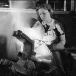 Image: A young woman welds a large metal bracket held in a vise