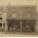 Image: Two men in Victorian attire stand in front of a two-storey brick and bluestone building