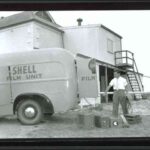 Image: A man in 1950s attire loads equipment into a panel van. The words ‘Shell Film Unit’ are painted on the side and back of the van