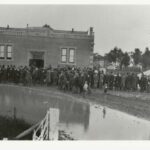 Image: A building with a large group of men gathered around the front.