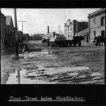 Image: Horse and cart and pedestrians on muddy unpaved roadway with stone and brick buildings either side