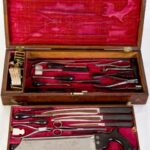 Image: Red velvet lined wooden box containing various 19th century medical instruments including forceps, knives and a saw