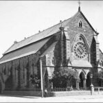 Image: A boy poses in front of the Baptist Church on the corner of Flinders Street and Divett Place. This church was built in 1861 to plans by Robert Thomas who also designed the Pilgrim Church. It features a rose window and front entrance with three arch