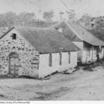 Image: Two gable roof, stone cottages sit adjacent to each other with the hills and gum trees of Lobethal in the background