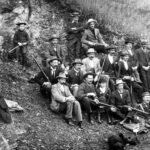 Group of rifle club members sitting together on a hill holding rifles