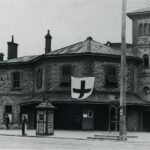 Image: Stone building on street corner with large entrance and fountain in front