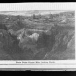 Image: A woodblock print of several buildings and chimneys arrayed at the top of a large open pit