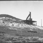 Image: A large chimney mounted on a wooden platform on the side of a hill. Several men stand at the base of the platform