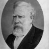 Image: A head-and-shoulders profile of a middle-aged man with white hair and beard. The man is wearing late-Victorian attire