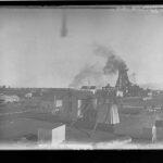 Image: Smoke billows from a steel tower surrounded by a number of buildings and an array of industrial equipment