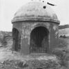 Black and white photo of concrete dome with arched entrances showing rocks inside